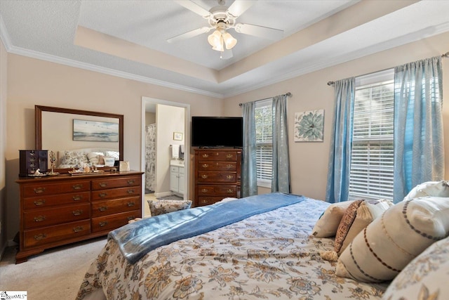 bedroom featuring a tray ceiling, ornamental molding, light colored carpet, ensuite bathroom, and ceiling fan