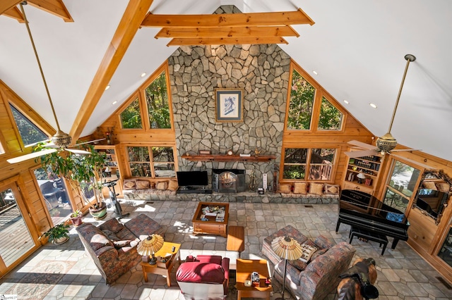 living room featuring beam ceiling, ceiling fan, high vaulted ceiling, wood walls, and a fireplace