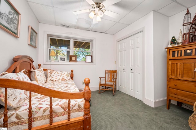 carpeted bedroom with a drop ceiling, ceiling fan, and a closet