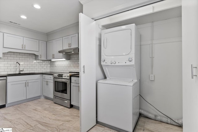 kitchen with crown molding, sink, stainless steel appliances, stacked washing maching and dryer, and decorative backsplash