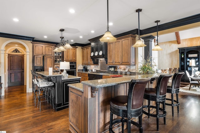 kitchen with a spacious island, a kitchen breakfast bar, stone counters, dark wood-type flooring, and pendant lighting