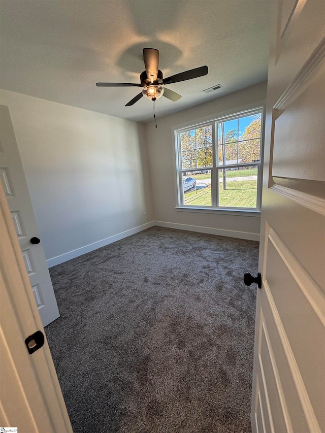 unfurnished room featuring ceiling fan, a textured ceiling, and dark carpet