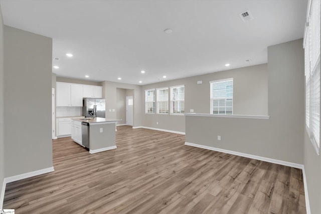 kitchen featuring appliances with stainless steel finishes, white cabinets, a center island with sink, and light wood-type flooring