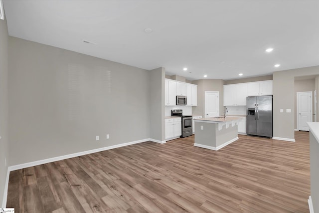 kitchen with sink, an island with sink, light hardwood / wood-style floors, stainless steel appliances, and white cabinets