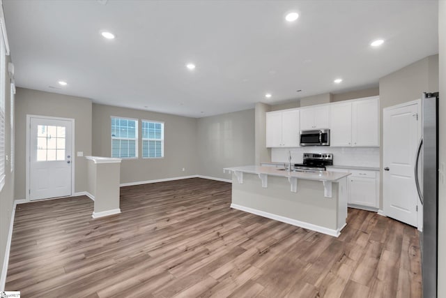 kitchen featuring white cabinets, a center island with sink, a kitchen breakfast bar, light hardwood / wood-style flooring, and stainless steel appliances