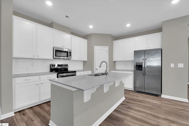 kitchen with sink, appliances with stainless steel finishes, light hardwood / wood-style floors, and an island with sink