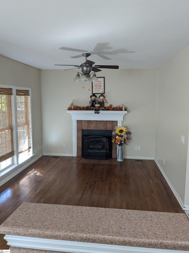 unfurnished living room with ceiling fan, dark hardwood / wood-style floors, and a tiled fireplace