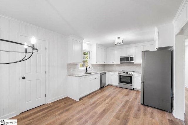 kitchen featuring appliances with stainless steel finishes, backsplash, white cabinetry, light hardwood / wood-style floors, and an inviting chandelier