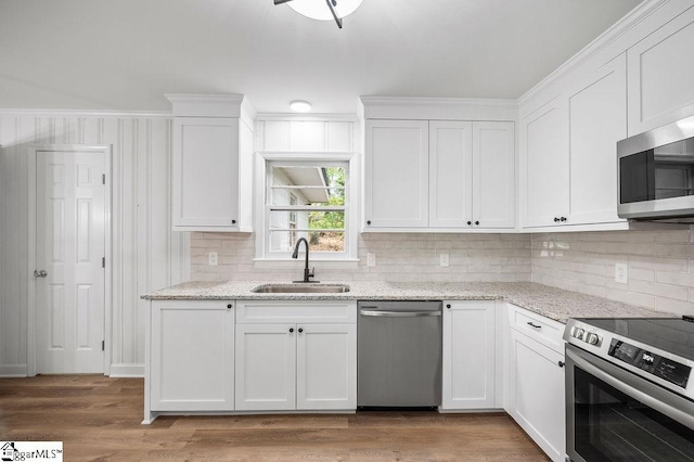 kitchen with appliances with stainless steel finishes, sink, wood-type flooring, white cabinetry, and light stone counters