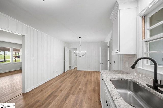 kitchen with sink, white cabinetry, light hardwood / wood-style flooring, and an inviting chandelier