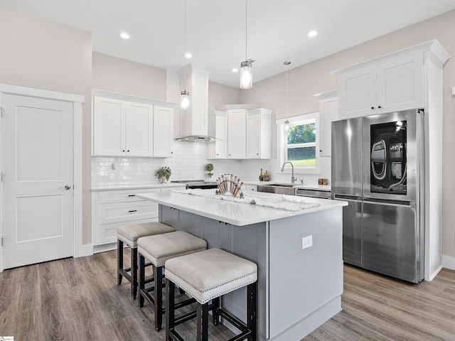 kitchen with stainless steel appliances, wall chimney exhaust hood, a center island, and white cabinets