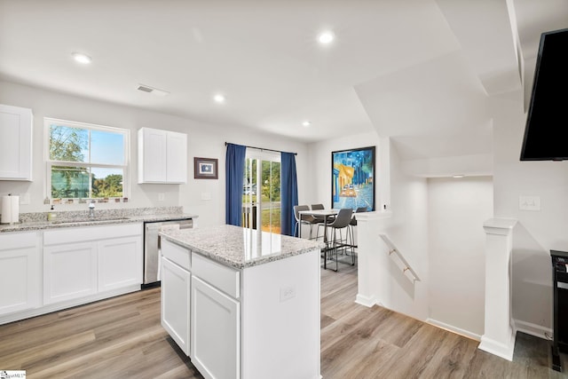 kitchen featuring stainless steel dishwasher, a center island, white cabinets, and light hardwood / wood-style floors