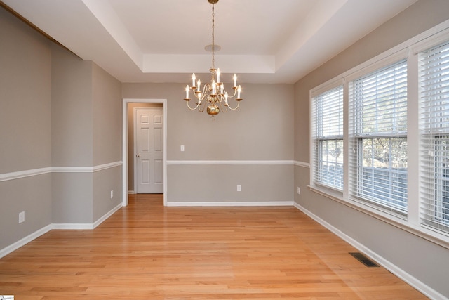 spare room featuring a notable chandelier, a tray ceiling, and light wood-type flooring