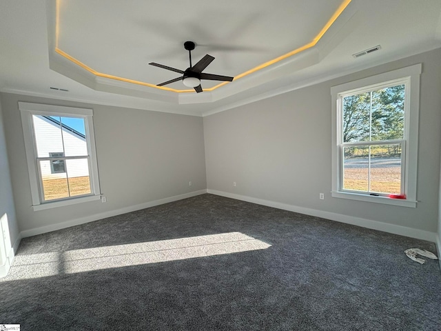 unfurnished room with dark carpet, plenty of natural light, a tray ceiling, and ceiling fan