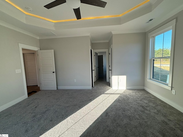 unfurnished bedroom with crown molding, a raised ceiling, dark colored carpet, and ceiling fan