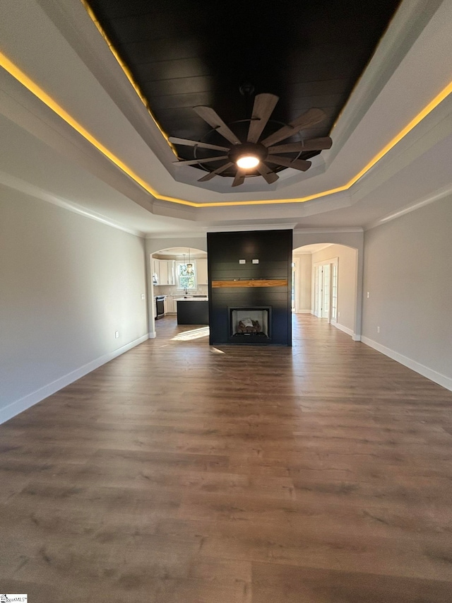 unfurnished living room featuring ceiling fan, a tray ceiling, and dark hardwood / wood-style floors