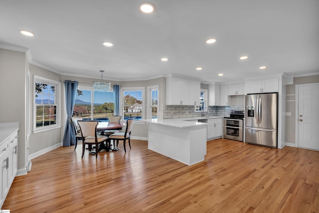 kitchen featuring a wealth of natural light, appliances with stainless steel finishes, hanging light fixtures, and white cabinets