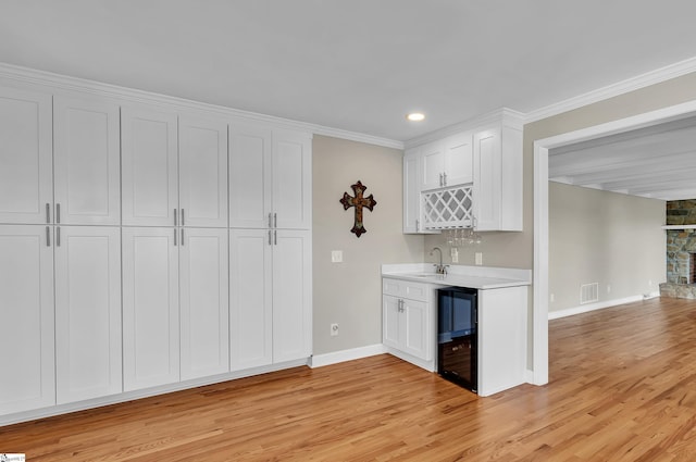 kitchen with wine cooler, white cabinetry, sink, and light hardwood / wood-style floors