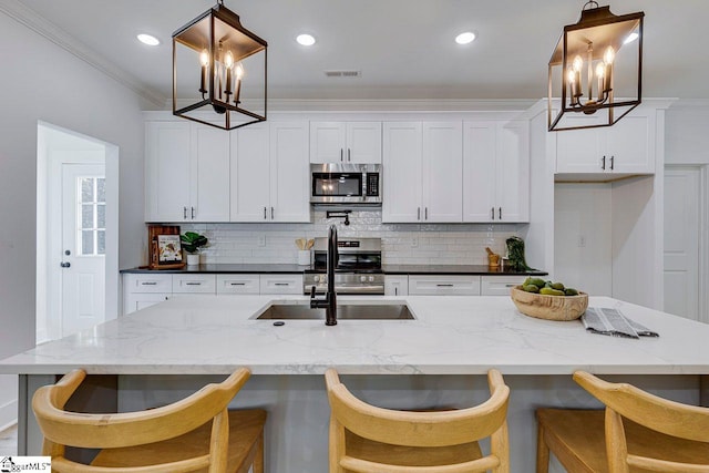 kitchen featuring a kitchen bar, hanging light fixtures, white cabinetry, stainless steel appliances, and a center island with sink