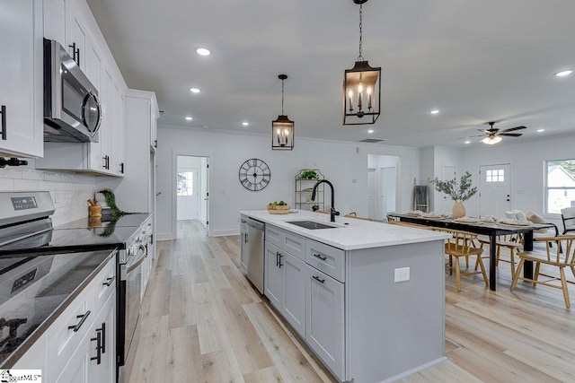 kitchen featuring appliances with stainless steel finishes, sink, white cabinetry, decorative light fixtures, and a kitchen island with sink