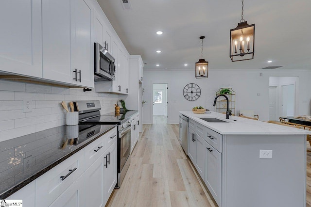 kitchen with a center island with sink, appliances with stainless steel finishes, decorative light fixtures, and white cabinets