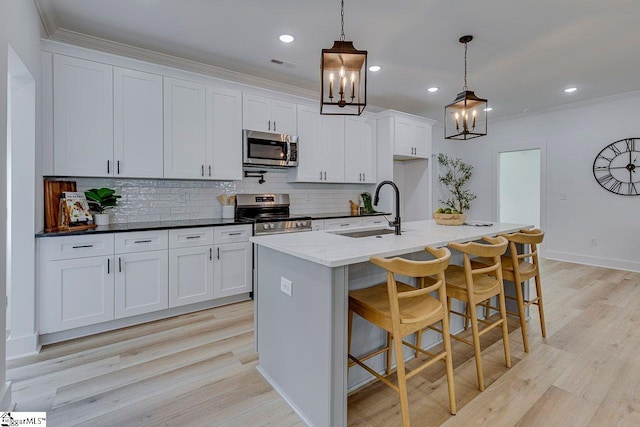 kitchen with pendant lighting, stainless steel appliances, an island with sink, and white cabinets