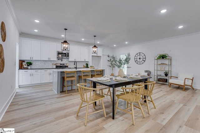 dining area with ornamental molding, sink, and light wood-type flooring