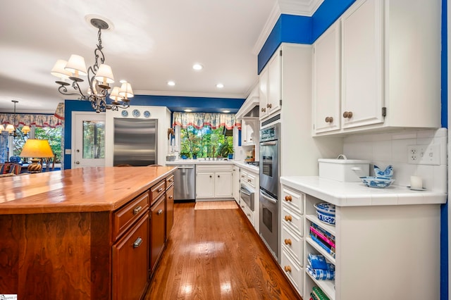 kitchen with stainless steel appliances, ornamental molding, dark hardwood / wood-style floors, and white cabinets