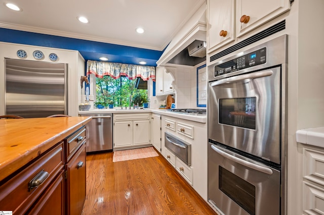 kitchen with backsplash, white cabinetry, light hardwood / wood-style floors, stainless steel appliances, and ornamental molding