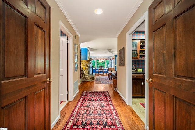 hallway with ornamental molding and light hardwood / wood-style floors