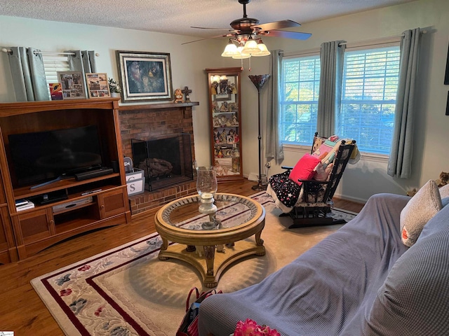 living room with a textured ceiling, hardwood / wood-style flooring, a fireplace, and ceiling fan