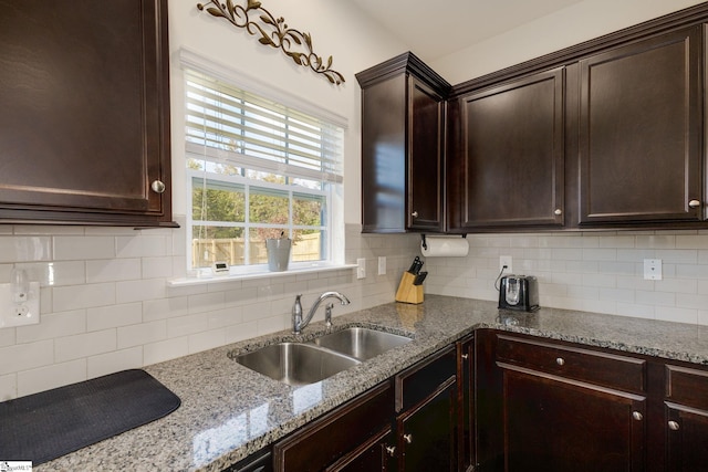 kitchen featuring dark brown cabinets, decorative backsplash, sink, and light stone counters