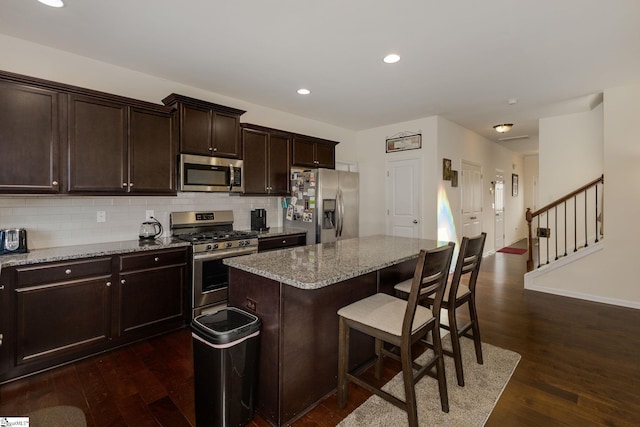 kitchen featuring a breakfast bar area, appliances with stainless steel finishes, a kitchen island, dark hardwood / wood-style flooring, and light stone counters