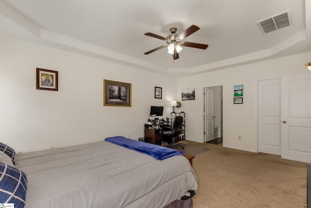 bedroom with ceiling fan, a raised ceiling, light carpet, and ensuite bathroom