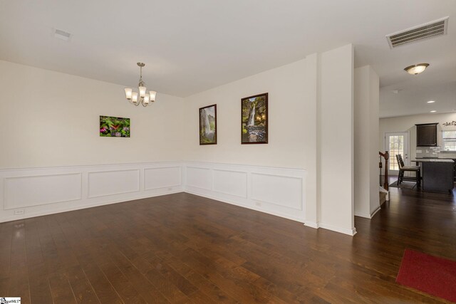 empty room with dark hardwood / wood-style flooring and an inviting chandelier