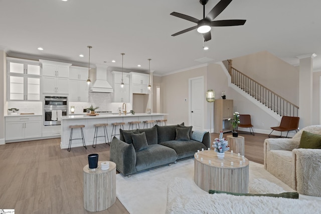 living room with crown molding, sink, ceiling fan, and light wood-type flooring