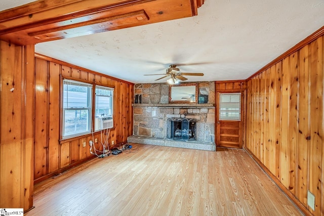 unfurnished living room featuring light hardwood / wood-style floors, wooden walls, a stone fireplace, and ceiling fan