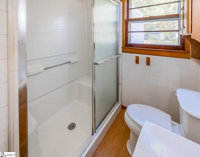 bathroom with a shower with door, tile walls, wood-type flooring, and toilet