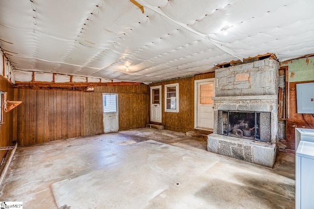 unfurnished living room with wood walls, electric panel, concrete flooring, and a fireplace