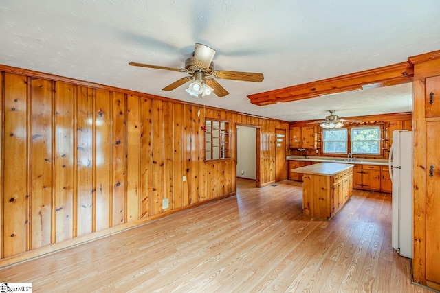 kitchen with wood walls, a kitchen island, light hardwood / wood-style floors, ornamental molding, and white refrigerator