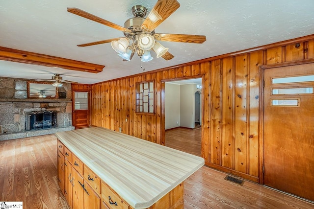 kitchen featuring crown molding, a stone fireplace, light hardwood / wood-style floors, and wood walls