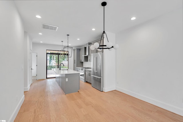 kitchen featuring high end appliances, a kitchen island with sink, sink, decorative light fixtures, and gray cabinets