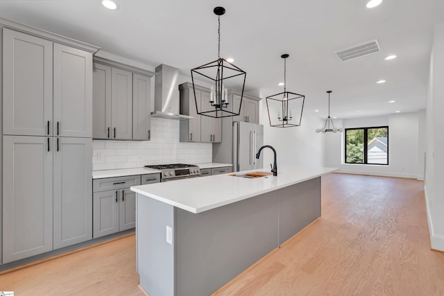 kitchen with a center island with sink, decorative light fixtures, gray cabinets, and wall chimney range hood