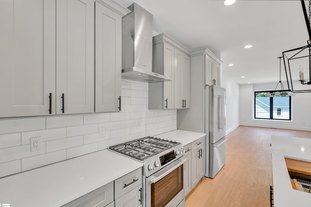 kitchen featuring wall chimney exhaust hood, high quality appliances, pendant lighting, decorative backsplash, and light wood-type flooring