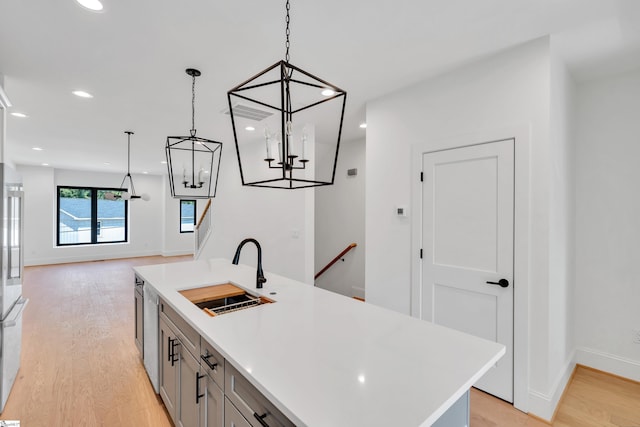 kitchen with gray cabinetry, sink, a center island with sink, light hardwood / wood-style flooring, and hanging light fixtures