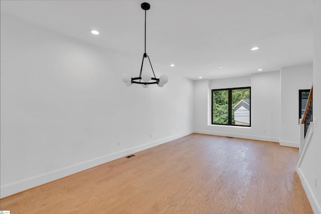 spare room with a notable chandelier and light wood-type flooring