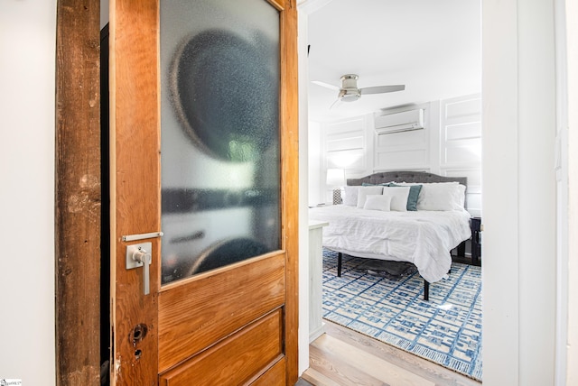 bedroom with an AC wall unit, light wood-type flooring, and ceiling fan