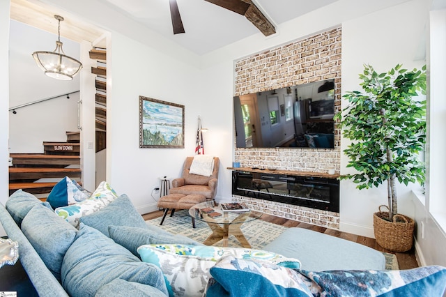 living room with beam ceiling, wood-type flooring, a brick fireplace, and ceiling fan with notable chandelier