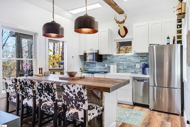 kitchen featuring butcher block countertops, white cabinetry, light hardwood / wood-style floors, stainless steel appliances, and a breakfast bar