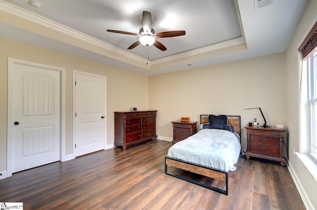 bedroom with crown molding, dark hardwood / wood-style floors, a tray ceiling, and ceiling fan